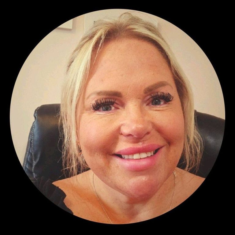 Smiling woman with blonde hair and long eyelashes, seated in a black chair.